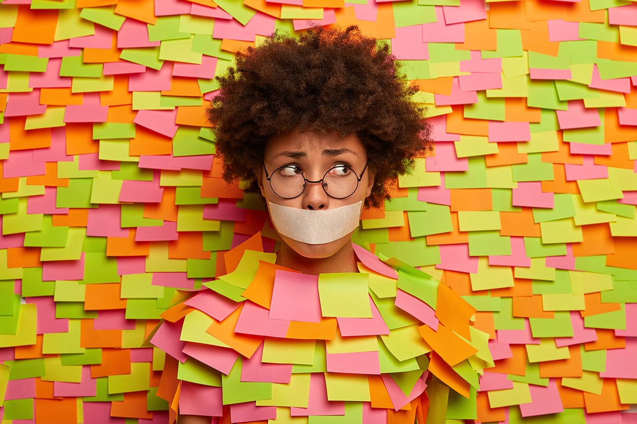 photo-puzzled-stressed-afro-woman-with-mouth-covered-by-tape-has-no-freedom-speech-being-kidnapped-looks-embarrassed-aside-wears-spectacles-poses-paper-wall-with-adhesive-notes